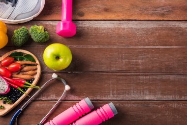 Kalp tabağında taze organik meyve ve sebzeler, ayakkabılar, spor malzemeleri ve doktor steteskopu, tahta spor masasında stüdyo çekimi, sağlıklı diyet vejetaryen gıda konsepti, Dünya Gıda Günü