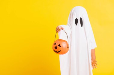 Komik cadılar bayramı çocuğu kavramı, beyaz kostümlü şirin çocuk Cadılar Bayramı hayaleti korkunç elinde turuncu kabak hayaleti, beyaz arka planda sarı bir stüdyo.