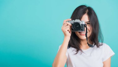 Gezgin turist mutlu Asyalı genç kadın yaz şapkasıyla gülümsüyor aynasız fotoğraf makinesiyle duruyor, mavi arkaplanda fotokopi alanı ile fotoğraf çekiyor.