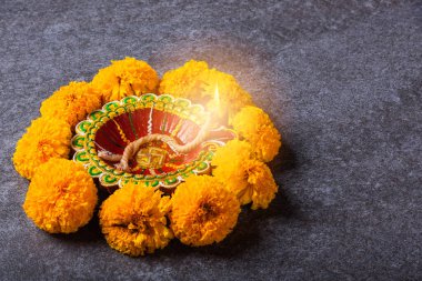 Üst tepedeki kil Diya 'yı ya da yağ lambasını ya da sarı çiçeği aydınlatıyor, stüdyo çekimleri somut arka planda, Hinduizm rangolisinin dekorasyonu, Mutlu Deepavali ya da Diwali festivali konsepti