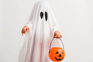 Komik Cadılar Bayramı Çocuğu kavramı, beyaz kostümlü küçük şirin çocuk Cadılar Bayramı hayaleti korkunç elinde turuncu kabak hayaleti, beyaz arka planda tek başına çekilmiş bir stüdyo resmi.