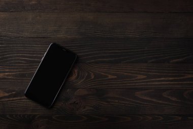 Siyah ahşap masa arkasındaki modern akıllı telefonun üst görüntüsünü fotokopi alanı ve cep telefonu boş ekran görüntüsüyle kapat