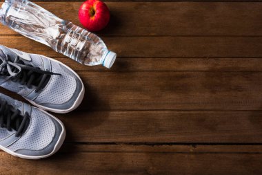 Spor ayakkabıları, şişe suyu ve ahşap masadaki kırmızı elma, spor salonundaki gri spor ayakkabıları ve aksesuar ekipmanları, sağlıklı spor konsepti.