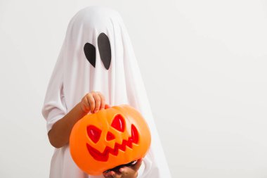 Komik Cadılar Bayramı Çocuğu kavramı, beyaz kostümlü küçük şirin çocuk Cadılar Bayramı hayaleti korkunç elinde turuncu kabak hayaleti, beyaz arka planda tek başına çekilmiş bir stüdyo resmi.