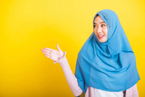 Asian Muslim Arab, Portrait of happy beautiful young woman Islam religious wear veil hijab funny smile she positive expression open palms with something on hand side space isolated yellow background