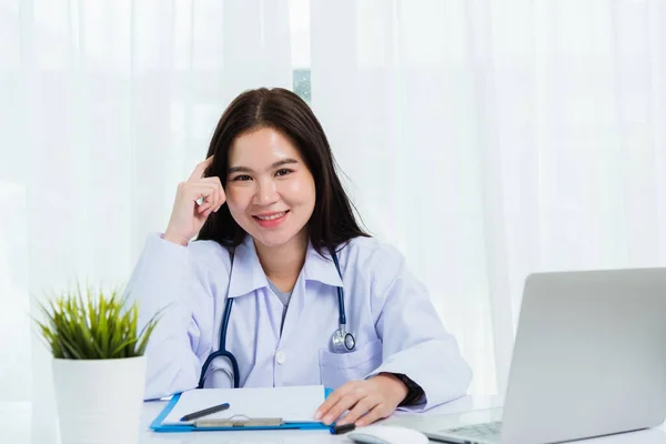 アジアの医師の若い美しい女性は ノートパソコンで作業を使用して笑顔と彼女は病院のデスクオフィスで書類やクリップボードの白い紙に何かを書く 医療の概念 — ストック写真
