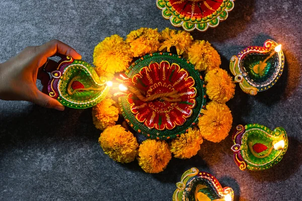 Close up woman hand being lit clay light fire on Diya or oil lamp studio shot on black wooden background, Decoration of Hinduism rangoli, Happy celebration Deepavali or Diwali festival concept