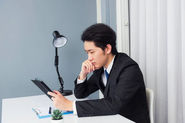 アジアの若いビジネスマンのビデオ会議コールや顔時間から仕事彼はスマートタブレットコンピュータを使用して机の上に座ってタブレットを見て笑顔と自宅のオフィスで利益のための仕事について考えて — ストック写真