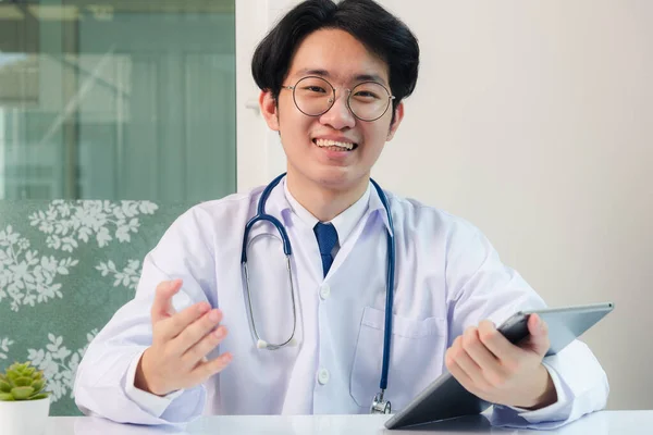 幸せなアジアの若い医師ハンサムな男性の笑顔は 眼鏡を着用現代のスマートデジタルタブレットコンピュータを使用して 病院のオフィスでのデスクで病気の患者の症状を説明します テクノロジーヘルスケアと医学 — ストック写真