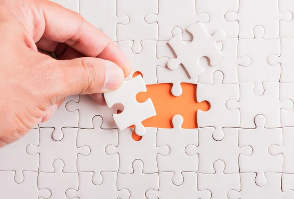 Top view flat lay of hand-holding last piece white paper jigsaw puzzle game last pieces put to place for solve problem complete mission, studio shot on an orange background, quiz calculation concept