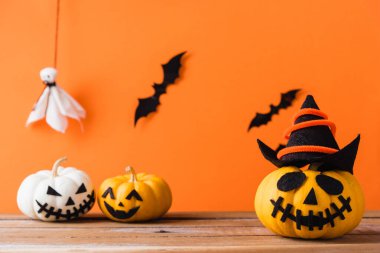 Komik Cadılar Bayramı dekorasyon partisi, şirin balkabağı hayaleti hayalet kabak fener maskesi şapka, siyah örümcek ve yarasalar ahşap masada, stüdyo çekimi turuncu arka planda, mutlu bayramlar konsepti