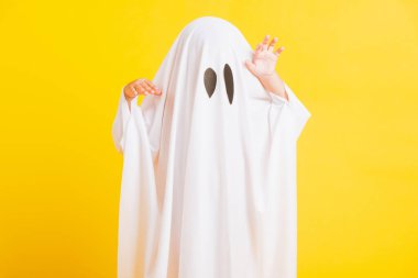 Komik cadılar bayramı çocuğu kavramı, yakın plan beyaz kostümlü küçük şirin çocuk cadılar bayramı hayaleti korkunç, sarı arka planda izole edilmiş stüdyo resmi.