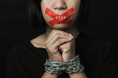 Asyalı bir kadın, ağzı kırmızı bantla kapatmış ve elleri siyah arka planda bağlanmış. Konuşma özgürlüğü sansürü ve konuşmayı durdurmak, Uluslararası İnsan Hakları Günü