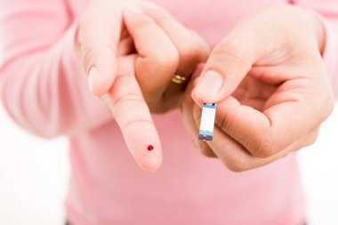Yakından bir kadın elinde glikoz testi seviyesini ölçen bir tabakla parmağında kan olan bir kadın yüksek kan şekeri diyabetini ve beyaz arka planda izole edilmiş glisemik sağlık konseptini izliyor.