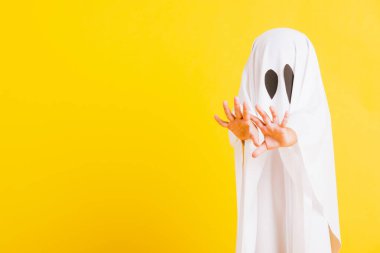 Komik cadılar bayramı çocuğu kavramı, yakın plan beyaz kostümlü küçük şirin çocuk cadılar bayramı hayaleti korkunç, sarı arka planda izole edilmiş stüdyo resmi.