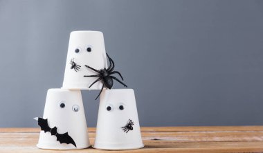 Komik el sanatları Cadılar Bayramı dekorasyon partisi, yakın plan kağıt bardak hayaleti, tahta duvardaki örümcek ve yarasalar gri arka plan ve fotokopi alanı, stüdyo çekimi izole edilmiş, mutlu tatiller konsepti