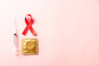 Kırmızı kurdele, HIV, AIDS kanseri farkındalığı, gölgeli kondom ve şırınga, pembe arka planda izole edilmiş stüdyo çekimi, sağlık sigortası cinsel konsepti, Dünya AIDS Günü