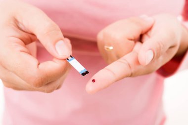 Yakından bir kadın elinde glikoz testi seviyesini ölçen bir tabakla parmağında kan olan bir kadın yüksek kan şekeri diyabetini ve beyaz arka planda izole edilmiş glisemik sağlık konseptini izliyor.