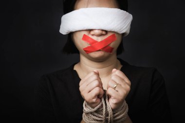 Köle gibi çalışan Asyalı kadın, kırmızı yapıştırıcı bantla gözlerini bağlıyor, zincirlerle bağlanıyor ve siyah arka planını kapatıyor. Konuşma özgürlüğü sansürü ve konuşmayı durdurmak, Uluslararası İnsan Hakları Günü