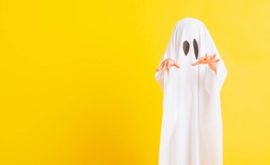 Komik cadılar bayramı çocuğu kavramı, yakın plan beyaz kostümlü küçük şirin çocuk cadılar bayramı hayaleti korkunç, sarı arka planda izole edilmiş stüdyo resmi.