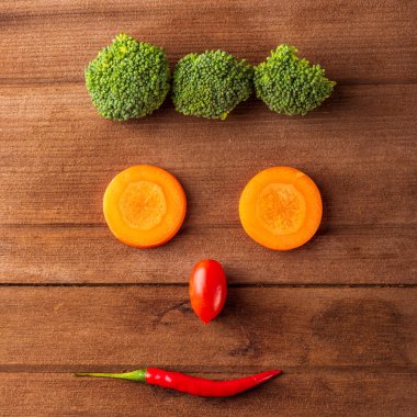 Tahta bir masa arkasında gülümseyen organik sebze ve meyve suratlı sağlıklı yaşam tarzı diyet gıda konseptinin üstüne yakın durun.