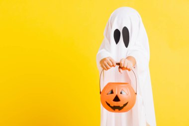 Komik cadılar bayramı çocuğu kavramı, beyaz kostümlü şirin çocuk Cadılar Bayramı hayaleti korkunç elinde turuncu kabak hayaleti, beyaz arka planda sarı bir stüdyo.