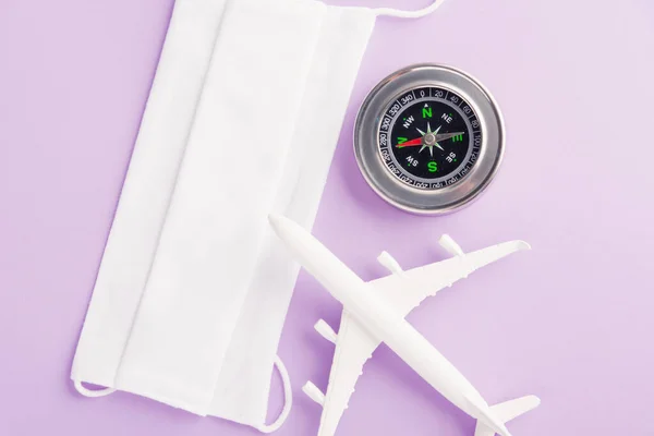 World Tourism Day, minimal toy model plane, compass and face mask protective pandemic coronavirus, studio shot isolated on a purple background, cancel flight holiday travel under COVID-19 concept