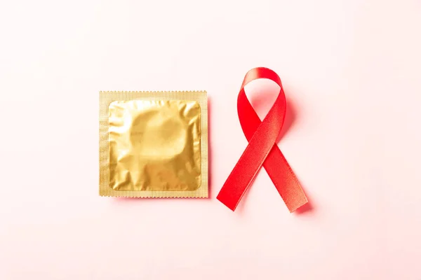 Red bow ribbon symbol HIV, AIDS cancer awareness and condom with shadows, studio shot isolated on pink background, Healthcare medicine sexually concept, World AIDS Day