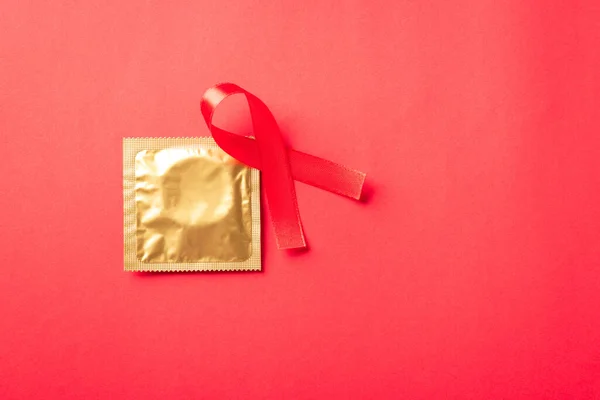 Red bow ribbon symbol HIV, AIDS cancer awareness and condom with shadows, studio shot isolated on red background, Healthcare medicine sexually concept, World AIDS Day