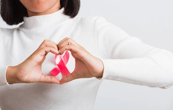 Breast cancer awareness healthcare and medicine concept. Close up Asian woman wear shirt she have pink breast cancer awareness ribbon on chest show symbol heart framing from fingers, white background