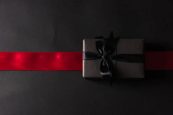 黑色星期五销售的概念 礼品盒顶部的视图包裹着黑色的纸和黑色的蝴蝶结压印 工作室拍摄和有红色的带子横跨黑暗的背景 — 图库照片