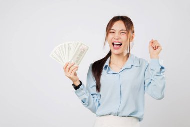Asyalı heyecanlı bir kadın elinde dolar ve hayran banknotları ile kutlama yapıyor. Yumruğunu kaldırıp, parasına gülerek, şans ve finansal başarısını kutluyor. Para birimi yükseltildi yumruk izole stüdyo beyaz arka plan
