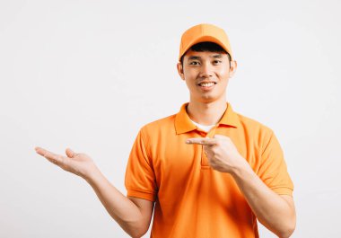 Asyalı gülümseyen genç teslimatçı, avuç içi stüdyolu, izole edilmiş beyaz arka plan, mutlu yaşam tarzı erkekler, mutlu ve pozitif ruh hali içinde, turuncu gömlekli birini taşıyor.