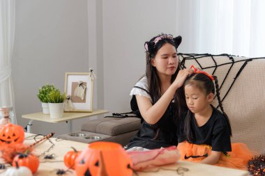 Kedi kulaklı bir kadın kız saçına turuncu bir kurdele takıyor ve ikisi de etrafında balkabağı ve bayram dekoru olan bir kostüm içinde neşeli bir cadılar bayramı için hazırlanıyorlar..