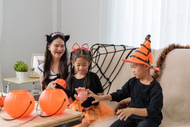 Kostümlü üç çocuk şeker toplamaya hazırlanıyor. Kardeşler kedi başlığı takıyor, balkabağı yayıyla sihirbaz şapkası takıyor. Balkabaklarının ve cadılar bayramı süslemelerinin yanında oturuyorlar..