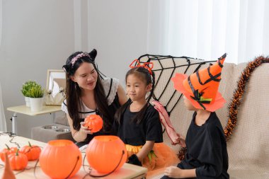 Aile tatilini kostümler içinde kutlar, cadı şapkası ve sahte kollu çocuklar, kadın Cadılar Bayramı için hazırlanan bir balkabağı tutar..