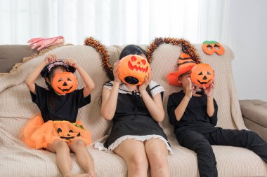 Üç kostümlü kız Cadılar Bayramı 'nda yüzlerine yanan balkabağı kovaları tutarlar. Turuncu çelenkler oturdukları koltuğu süslerler. Arkalarında şenlikli süsler mutlu bir sahne oluşturur..