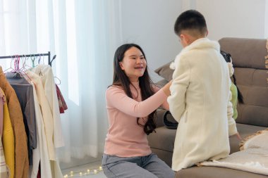 Gülümseyen bir kadın, bir çocuğun soğuk bir kış günü için hazırlanmasına yardım ediyor. Yavrunun üzerine kalın bir palto giymesine yardım ediyor..