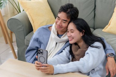 Winter couple, happy family people indoor home, warm bonding activity for young adults. Two people enjoy cozy winter day, sharing sweet selfie on smartphone, creating lovely memory.