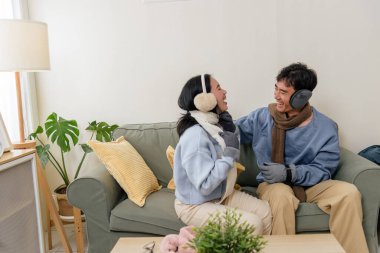 Winter day, happy couple enjoys cozy home indoor fun, people laugh together wearing warm clothes, feeling comfort and joy in relaxed setting, creating joyful memories during cold winter season.