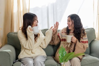 Winter day finds happy women friends at home, enjoying cozy friendship with warm drinks, laughing, sharing stories inside warm home during brisk winter season.