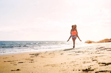 Mutlu sevgi dolu aile anne ve kızı çalıştıran ve sahip eğlenceli gün batımında - sahilde anne omzunda çocuğunu okyanus yanındaki - üst, tatil sırasında aile yaşam tarzı kavramı