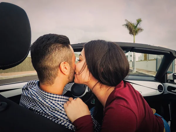 Young couple kiss in a convertible car during their road trip - Happy romantic newlywed date driving a cabriolet auto in honeymoon - Love, relationship and youth holidays lifestyle