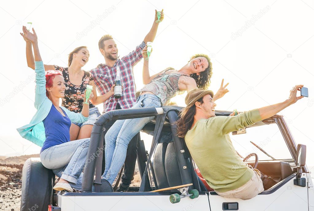 Group of happy friends taking selfie with mobile smart phone on convertible car - Young people having fun making party during their road trip - Friendship, vacation, youth holidays lifestyle concept