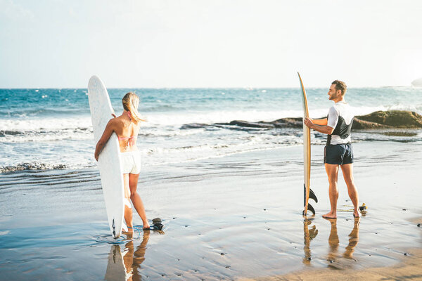 Young couple of surfers standing on the beach with surfboards preparing to surf on high waves - Sporty people having fun during a surfing day - Extreme sports, relationship and youth lifestyle concept