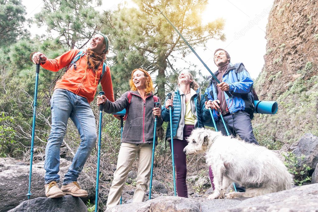 Group of friends with backpacks doing trekking excursion on mountain with their pet - Young tourists walking and exploring the wild nature - Trekker, hike and travel people concept