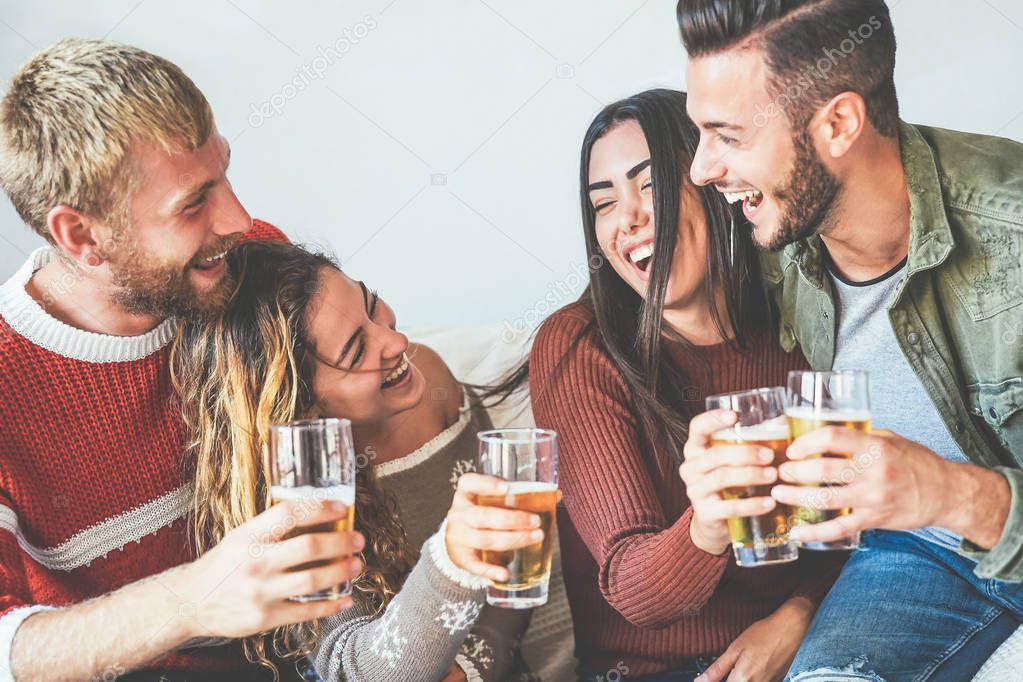 Group of happy friends cheering with beer at home - Millennial Young people having fun drinking and laughing together sitting on sofa - Friendship, entertainment and youth lifestyle holidays