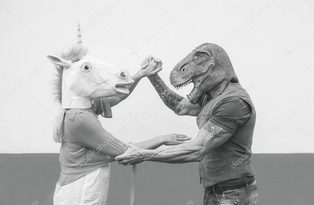 Crazy couple dancing and wearing dinosaur and unicorn mask - Senior trendy people having fun masked at carnival parade - Absurd, eccentric, surreal, fest and funny masquerade concept
