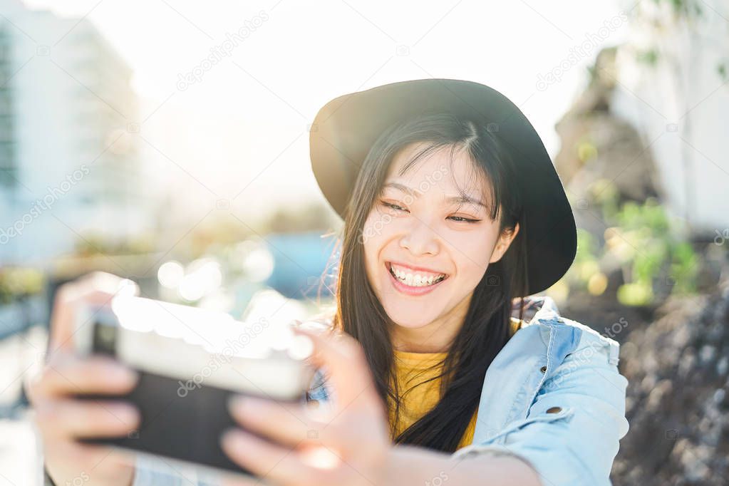 Happy Chinese influencer woman doing photo on vacation - Young trendy Asian girl taking selfie outdoor - People, photography, millennials, technology and youth lifestyle concept