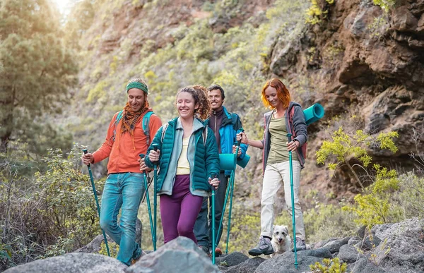 Group of friends with backpacks doing trekking excursion on mountain - Young tourists walking and exploring the wild nature - Trekker, sport, hike and travel concept